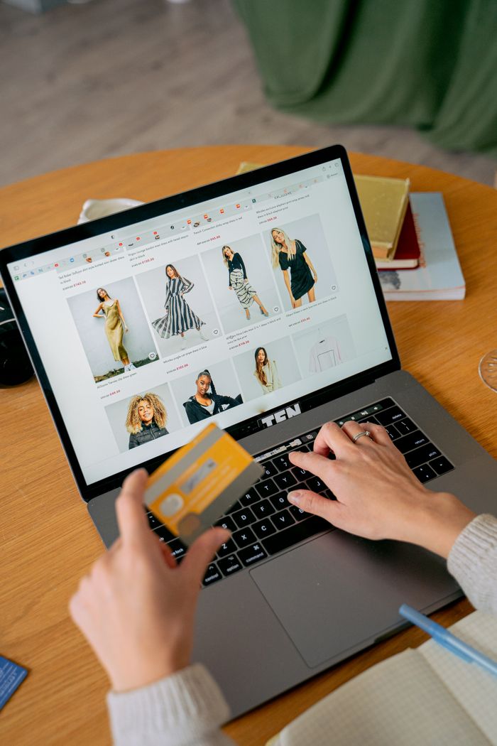 services-01 A woman makes an online purchase using a credit card on her laptop, browsing an online fashion store.